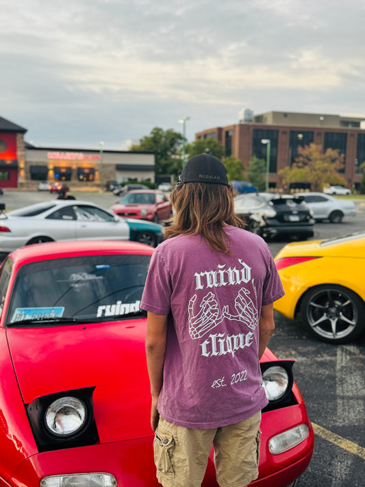 Berry t-shirt from the back, featuring the 'Ruind Clique' club name and two skeleton hands linked together. The scene is set in front of a lineup of stylish cars, adding a bold and urban aesthetic.