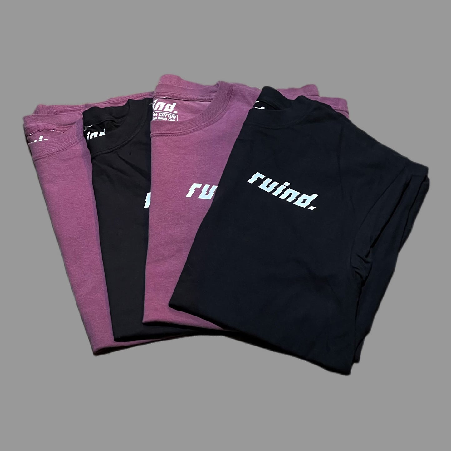 Front view of four t-shirts: two berry t-shirts and two black t-shirts, each featuring the 'Ruind Clique' logo on the left chest pocket. Simple yet bold designs highlighted against a clean backdrop.