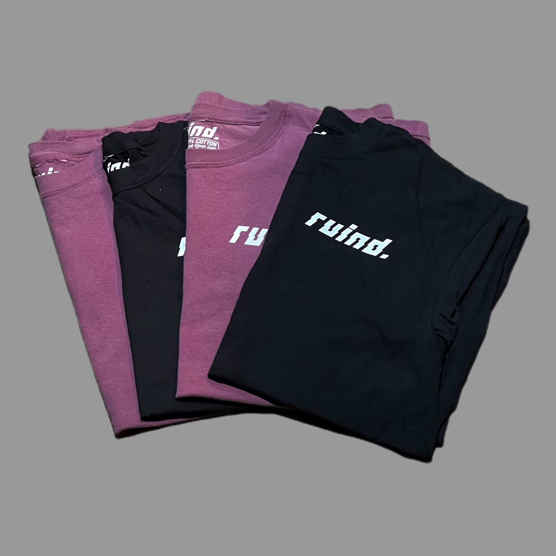 Front view of four t-shirts: two berry t-shirts and two black t-shirts, each featuring the 'Ruind Clique' logo on the left chest pocket. Simple yet bold designs highlighted against a clean backdrop.